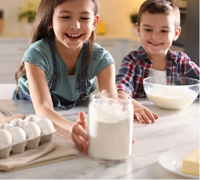 a young girl and boy mix baking ingredients on a granite countertop